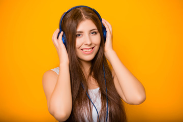 Close Up portrait of a beautiful, young woman listening to music with headphones, standing on a yellow background.