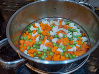 Hot and steaming freshly boiled peas, beans, carrots and cauliflower being strained through a stainless steel colander prior to serving for dinner