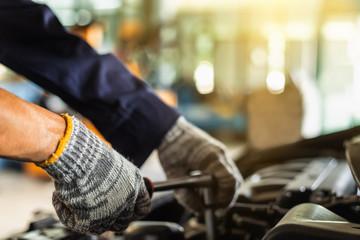 Close up, Asian man auto mechanic using a wrench and screwdriver to working service car in garage.