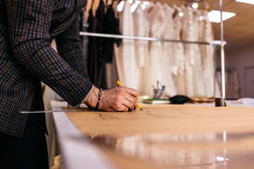Young serious tailor with beard looking at drawing near wooden table with threads in amazing atelier with antique furniture and mannequin