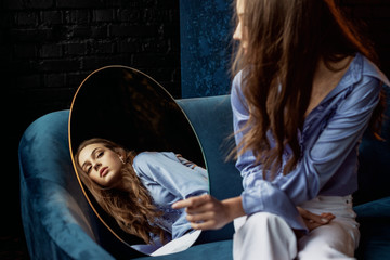 Young elegant beautiful fashionable brunette woman with long hair looking in the mirror. Model...