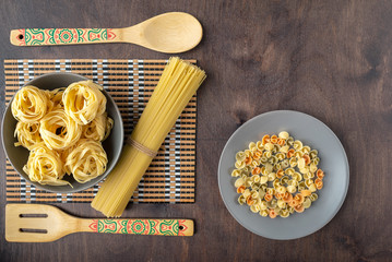 fettuccine paste on a grey plate on a bamboo substrate and wooden spatulas and multicolored paste...