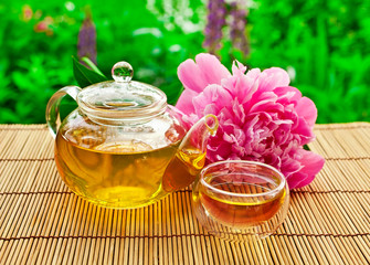 Glass teapot of green tea  with glass cup and pink peony flower.