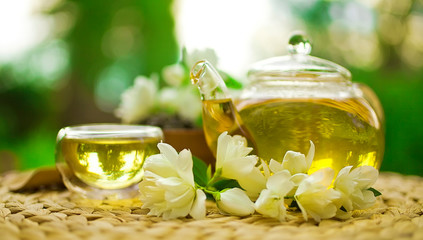 Jasmine green tea in a glass teapot with a glass cup and fresh blossoms.