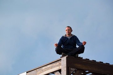 Fototapeta premium Young athletic man meditating, against blue sky background