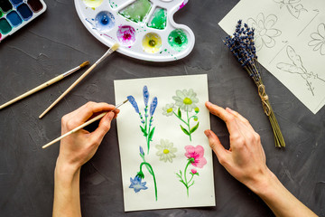 Painting. Female hands draw flowers on grey background top-down