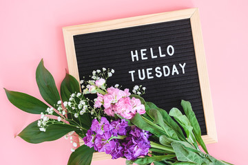 Hello Tuesday text on black letter board and bouquet colorful flowers on pink background. Concept Happy Tuesday. Template for postcard, greeting card Flat lay Top view