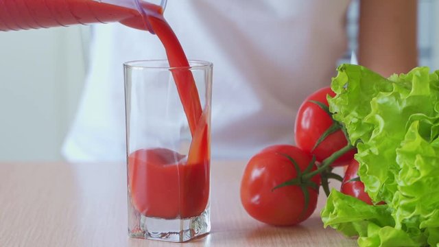 Tomato juice pouring from jug into a glass.