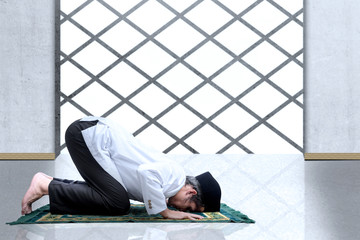Asian Muslim man with a prayer rug in a praying position (salat)