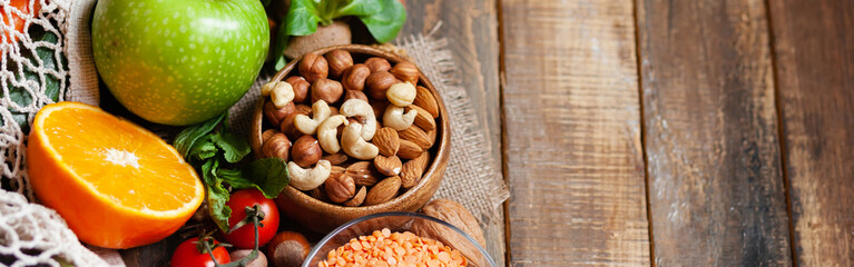 Concept of healthy vegan food, clean eating. Fresh raw ingredients on wooden background: vegetables, fruits, nuts, beans and lentils. No plastic, eco-friendly shopping, zero waste. Banner, copy space