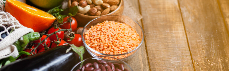 Concept of healthy vegan food, clean eating. Fresh raw ingredients on wooden background: vegetables, fruits, nuts, beans and lentils. No plastic, eco-friendly shopping, zero waste. Banner, copy space