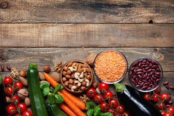 Concept of healthy vegan food, clean eating. Fresh raw ingredients on wooden background: vegetables, nuts, beans and lentils.Flat lay, top view, copy space for text