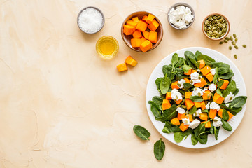 Salad with pumpkin and basil - near ingredients - on beige background top-down copy space