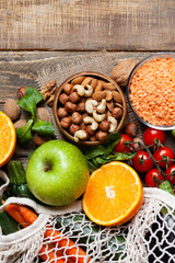 Concept of healthy vegan food, clean eating. Fresh raw ingredients on wooden background: vegetables, fruits, nuts, beans and lentils. Eco-friendly shopping, zero waste. Copy space, flat lay, top view