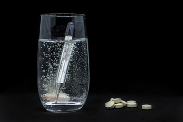 glass of water , thermometer and pills isolated on black background.