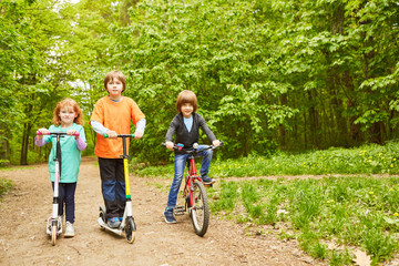 Obraz premium Drei Kinder mit Roller und Fahrrad im Park