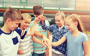 primary education, friendship, childhood and people concept - group of happy elementary school students with hands on top outdoors