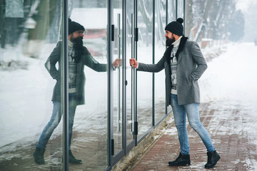 Handsome stylish man opens the door to shop. Fashion man in a winter coat outdoors