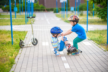 two boys in park, help boy with roller skates to stand up