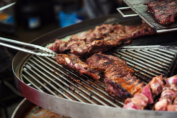 Chef preparing meat on the grill. Food catering, party. Street festival. Barbeque, BBQ concept. Male hand with tongs holding hot pork ribs. Street food.