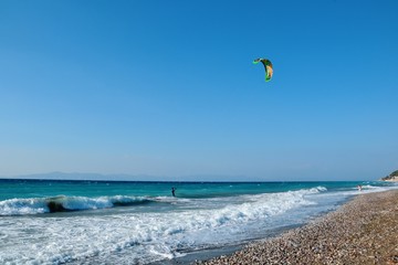 Ixia, Rhodes, Greece. A kiteboarder harnesses the power of the wind with a large controllable power kite to be propelled across the sea water. Pebble beach in Paralia/Ixia