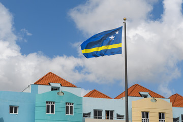 The blue-yellow Flag of Curacao Island (Netherlands Antilles) flutters in the blue cloudy sky above...
