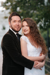 Beautiful wedding couple of newlyweds - red-haired young bride in a white dress and a bearded groom in a black suit. Amazing smiling wedding couple. Pretty bride and stylish groom.