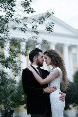 Beautiful wedding couple of newlyweds - red-haired young bride in a white dress and a bearded groom in a black suit. Amazing smiling wedding couple. Pretty bride and stylish groom.