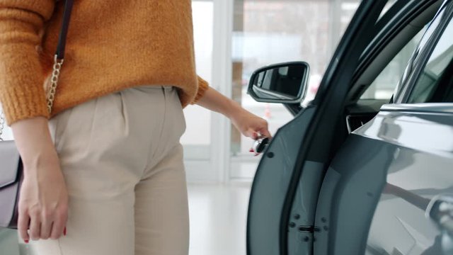 Close-up of anonymous female buyer opening car door looking inside choosing automobile in dealership. Shopping and modern transport concept.