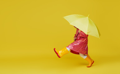 Cheerful child girl with yellow umbrella and red rain coat on colored yellow background. Copy space for text