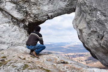 Young hiker looking through natural window in cliff. Tourist enjoy in natural wonders in mountains in spring