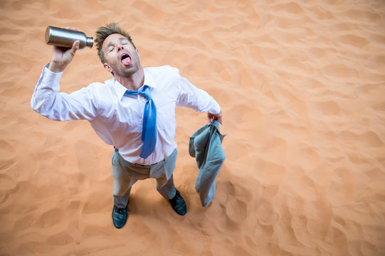 Thirsty businessman standing on red sand desert pouring an empty water bottle over his tongue