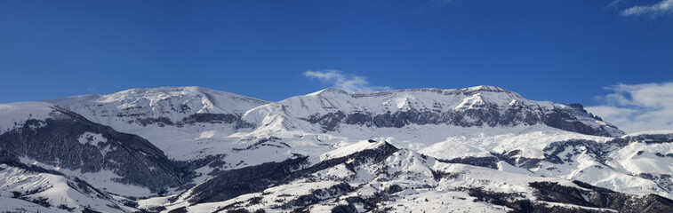 Panorama of high snowy mountains and blue sky with clouds at sun winter day
