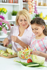 Cute little girl with her mother cooking together at kitchen table