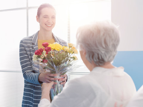 Woman Visiting A Senior Patient And Giving Her Flowers