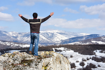 Tourist man is feeling free and standing with hands up on the top of the mountain. Climber enjoy in...