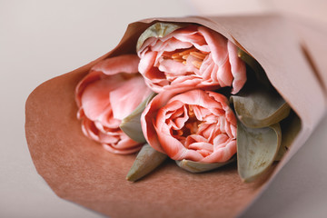 A bouquet of three tulips in a paper wrapper lies on a table. Close up view, tinted version