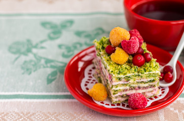 Spinach cream cake with cranberry and raspberry berries on a red plate, copy space