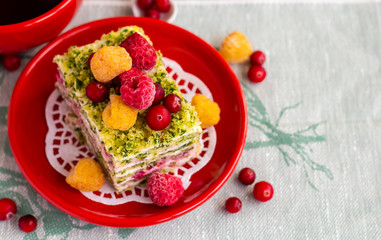 Spinach and raspberry cake decorated with berries on a red plate, copy space