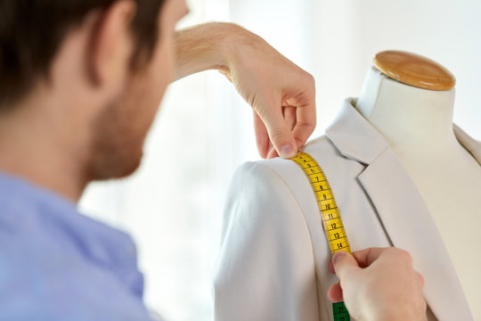 tailoring, sewing and clothing concept - close up of male fashion designer measures jacket with tape measure