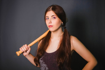 Obraz premium Young beautiful woman with a baseball bat in her hands. Fashionable studio photo on a gray background in the gangster style. Casual wear. Model with clean skin.
