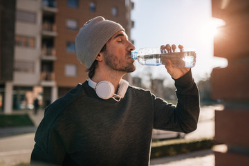 Fototapeta na wymiar Young athletic man with eyes closed drinking water outdoors.