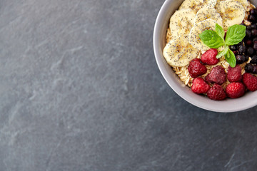 food and breakfast concept - oatmeal cereals in bowl with wild berries, banana and peppermint on slate stone table