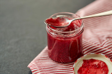 food, preserves and eating concept - mason jar with red raspberry jam and spoon on towel