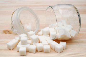 sugar cubes spilled from overturned glass sugar bowl  on wooden background