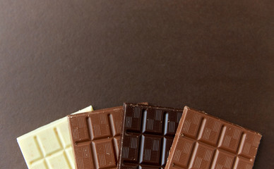 sweets, confectionery and food concept - milk, dark and white chocolate bars on brown background