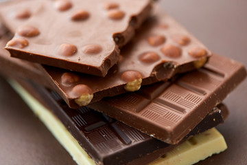 sweets, confectionery and food concept - bars of dark, white and milk chocolate with nuts on brown background