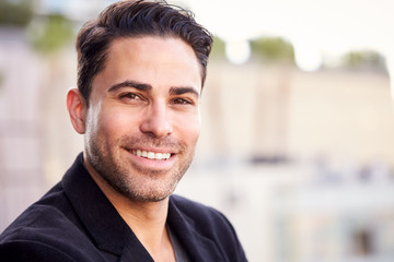 Portrait Of Smiling Businessman Standing Outside Office Building With City Skyline In Background