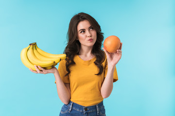 Thoughtful woman choosing between bananas and orange.