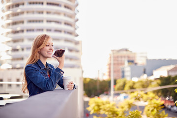 Fototapeta premium Businesswoman Standing Outside Office Building Using Mobile Phone With City Skyline In Background